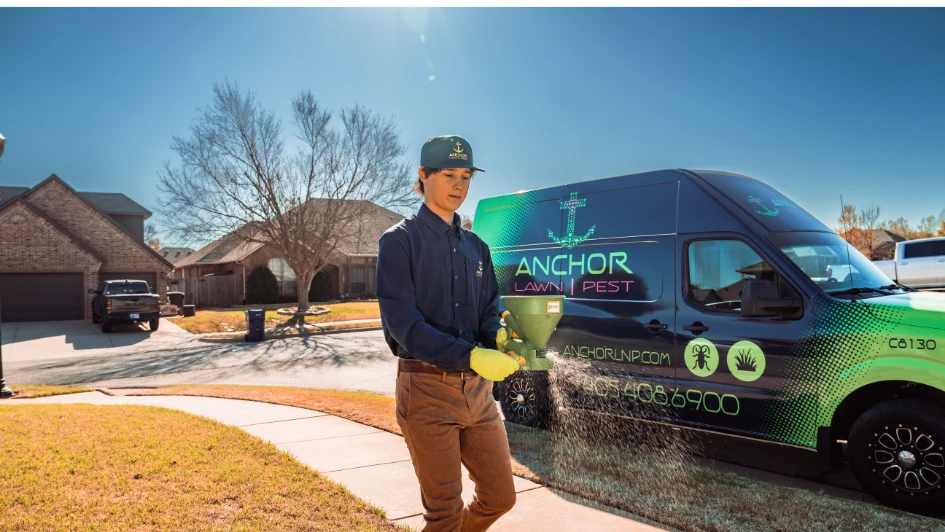 Lawn technician applying granular treatment beside a branded service van