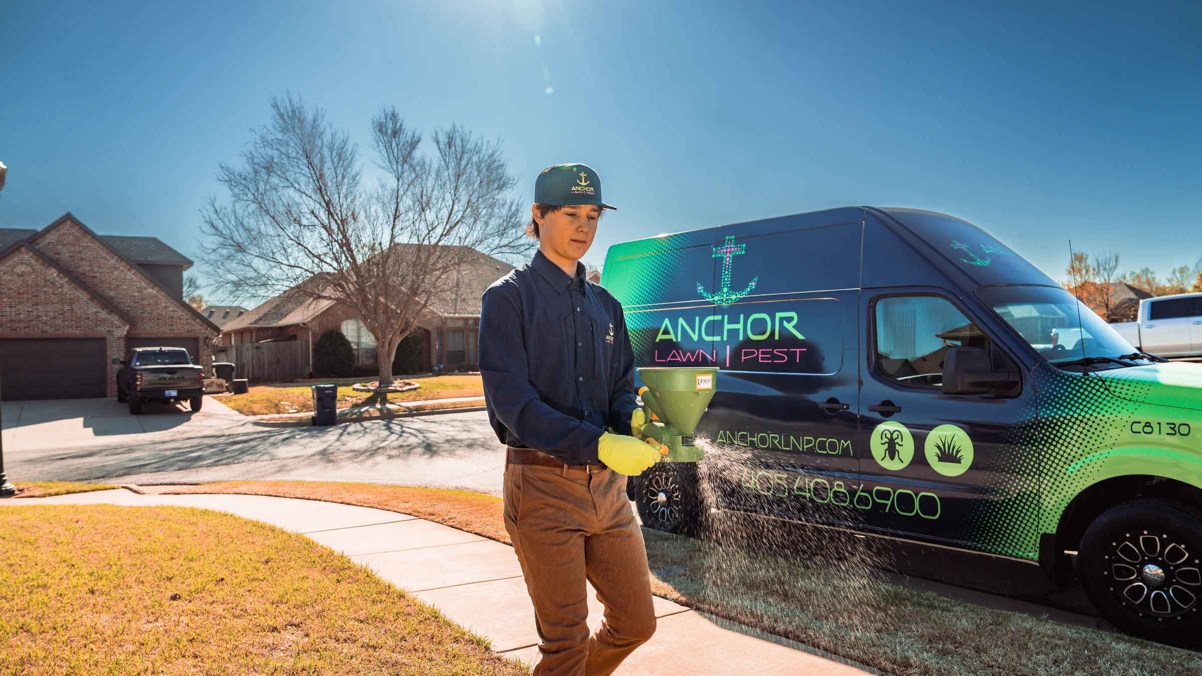 Technician applying granular material on a lawn beside a branded service van