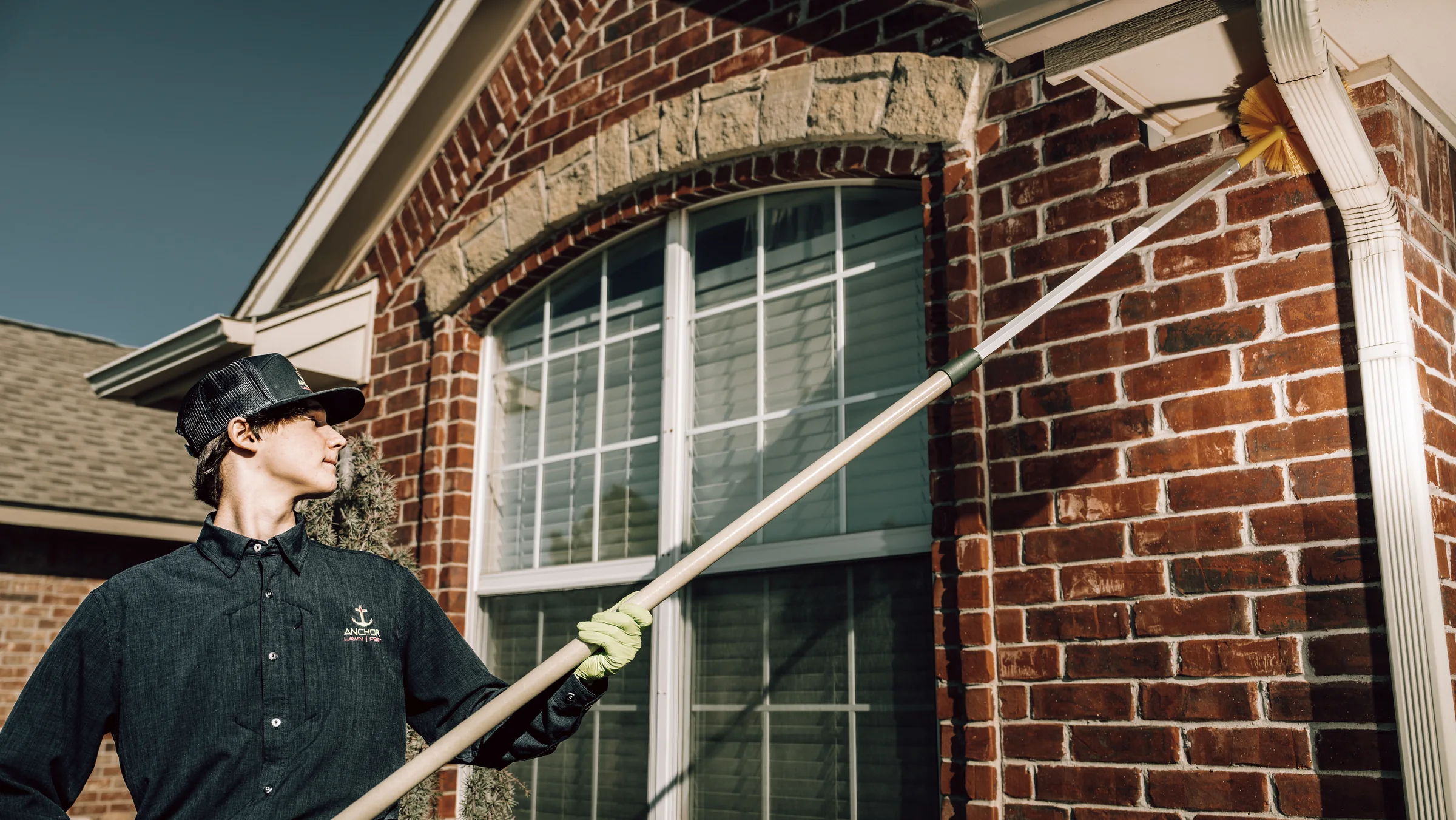 Pest technician applying a targeted treatment along the eaves of a brick home